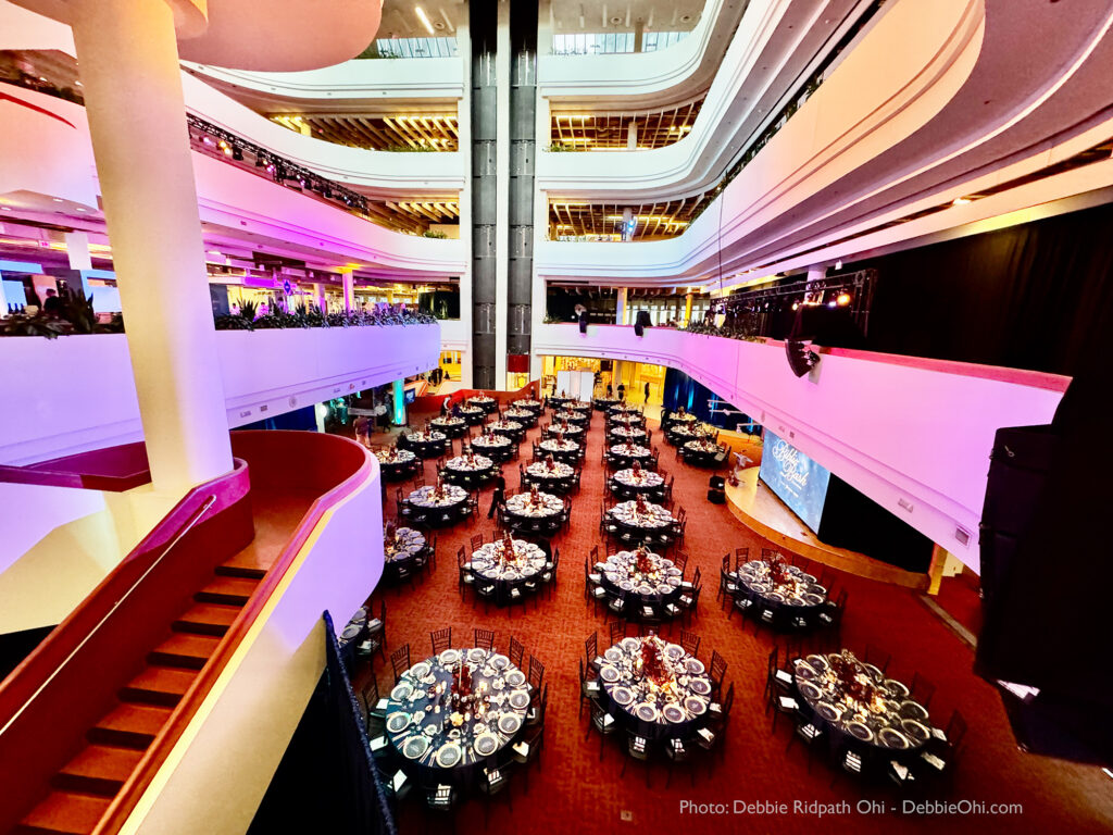 Interior of a large space with multiple floors and a central open atrium. The first floor is filled with round tables with formal dining settings.