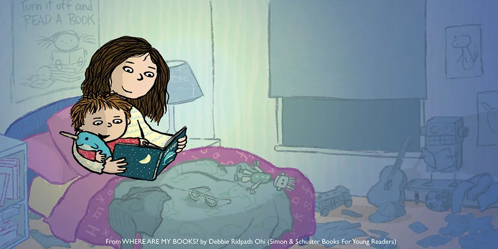 Illustration of a woman sitting on a child’s bed, reading a book to a boy who is holding a stuffed animal. The bedroom is dimly lit, with posters on the wall, toys, and musical instruments on the floor. Text at the bottom: “From WHERE ARE MY BOOKS? by Debbie Ridpath Ohi (Simon & Schuster Books For Young Readers).”