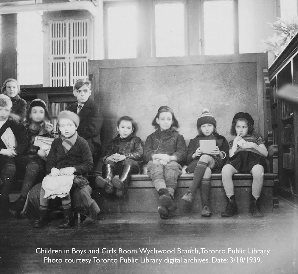 Black-and-white photo of children sitting on benches holding books in the Boys and Girls Room, Wychwood Branch, Toronto Public Library. Caption notes the photo is from the Toronto Public Library digital archives, dated March 18, 1939.